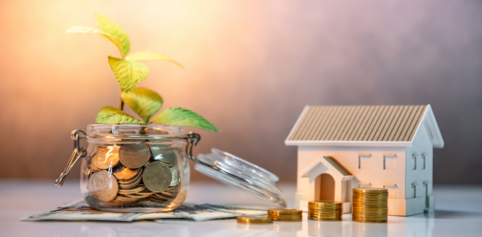 Glass jar filled with coins and plant growing out of it and little model house