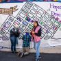 Three young people painting a mural on the street. One of the artists is holding a paintbrush while looking directly at the camera. The mural is a map of the Tenderloin neighborhood. 