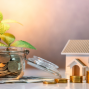 Glass jar filled with coins and plant growing out of it and little model house